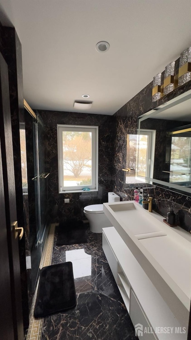 bathroom with walk in shower, vanity, toilet, and tile walls