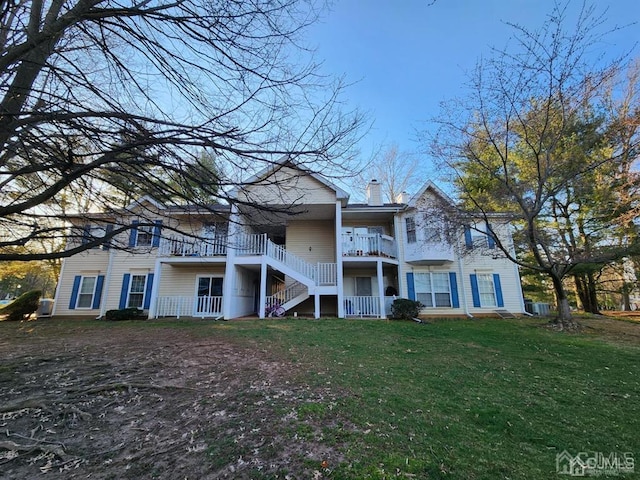 view of front of house featuring a balcony, a chimney, stairs, and a front lawn