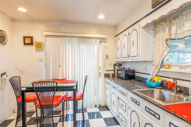 kitchen featuring dark countertops, recessed lighting, white cabinets, a sink, and tile patterned floors