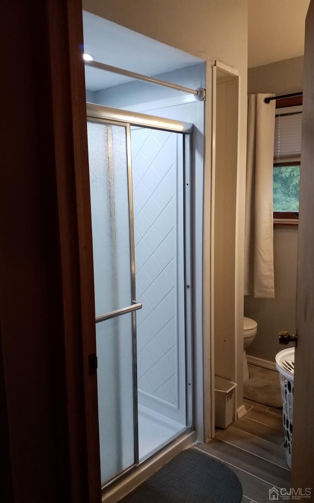 bathroom featuring hardwood / wood-style flooring, a shower with door, and toilet