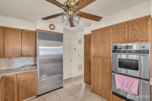 kitchen featuring stainless steel appliances, a warming drawer, brown cabinets, ceiling fan, and light tile patterned floors