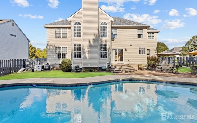 rear view of property with a fenced in pool, a yard, and a patio