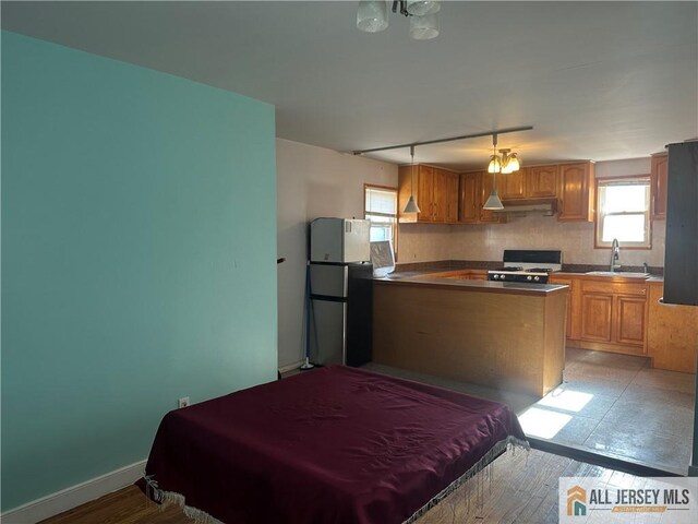 kitchen with hanging light fixtures, kitchen peninsula, refrigerator, sink, and white gas stove