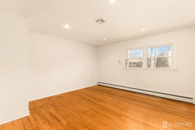 spare room featuring baseboard heating and light hardwood / wood-style flooring