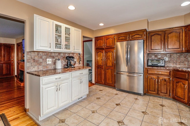 kitchen with decorative backsplash, stainless steel fridge, dark stone counters, and light hardwood / wood-style flooring