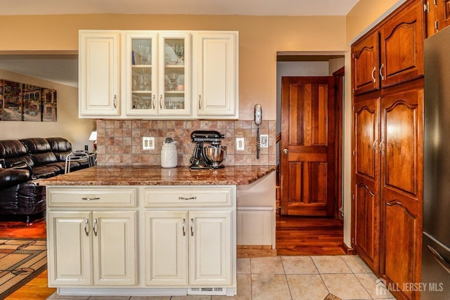 kitchen with light hardwood / wood-style floors, stainless steel refrigerator, dark stone counters, and tasteful backsplash