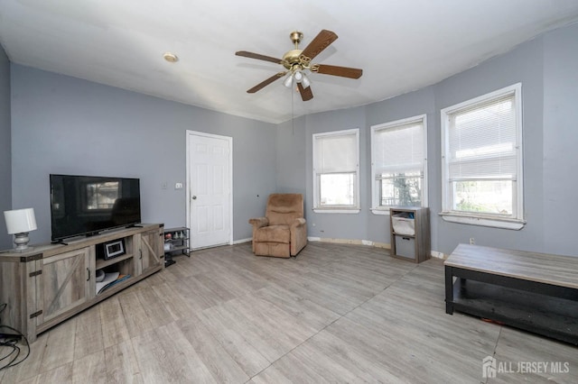 living area with light wood-style floors, a ceiling fan, and baseboards