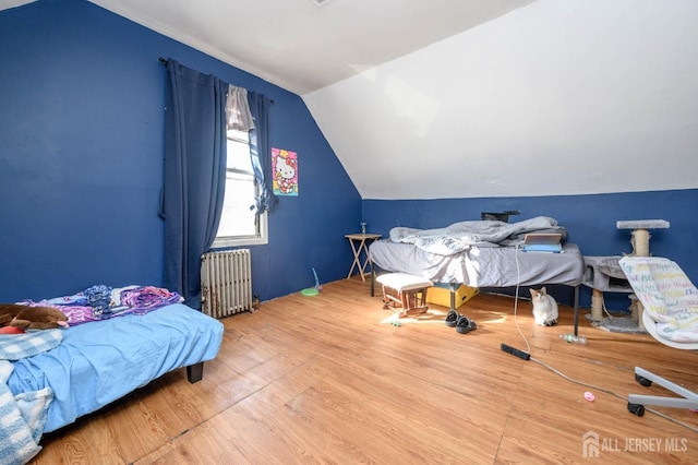 bedroom with lofted ceiling, radiator heating unit, and wood finished floors