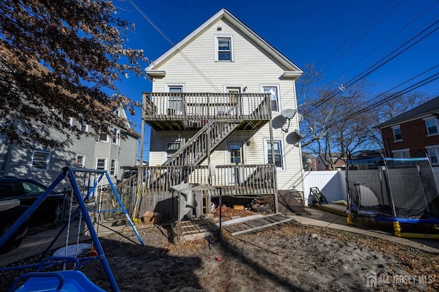 rear view of house featuring a trampoline, fence, a deck, and a playground