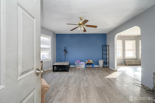 game room with arched walkways, baseboards, radiator heating unit, and wood finished floors