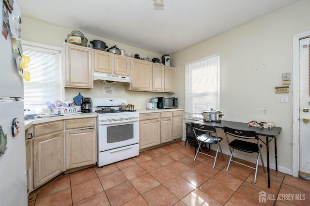 kitchen featuring under cabinet range hood, white gas range, light tile patterned floors, and light brown cabinetry