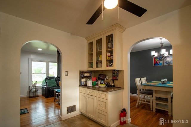 kitchen featuring arched walkways, ceiling fan, glass insert cabinets, decorative backsplash, and a chandelier