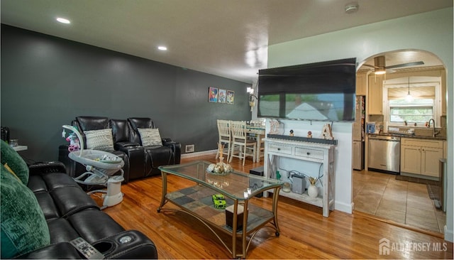 living room with arched walkways, a ceiling fan, light wood finished floors, recessed lighting, and baseboards