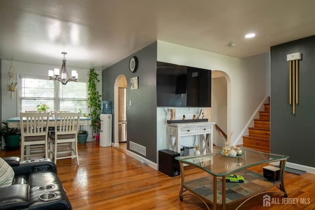 living area with arched walkways, stairway, light wood finished floors, and a chandelier