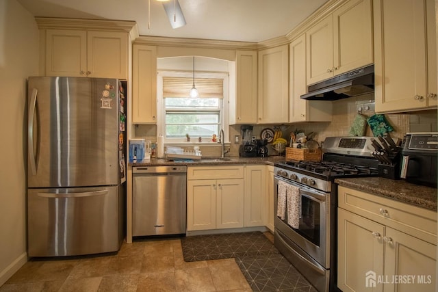 kitchen with appliances with stainless steel finishes, under cabinet range hood, cream cabinets, a sink, and tasteful backsplash