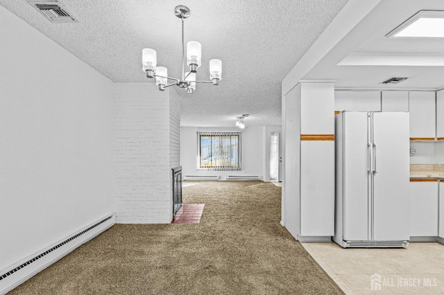 unfurnished dining area featuring a brick fireplace, a textured ceiling, light colored carpet, a baseboard radiator, and an inviting chandelier