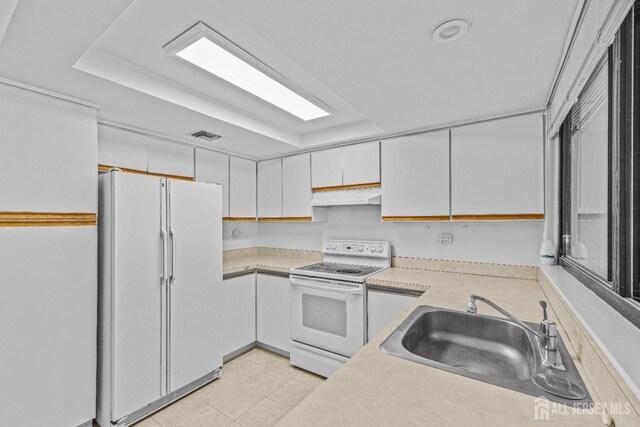 kitchen featuring a raised ceiling, white appliances, white cabinetry, and sink