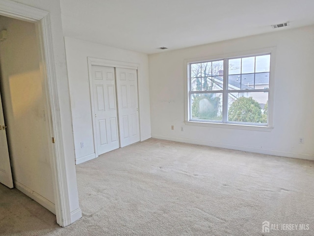 unfurnished bedroom with baseboards, visible vents, a closet, and light colored carpet