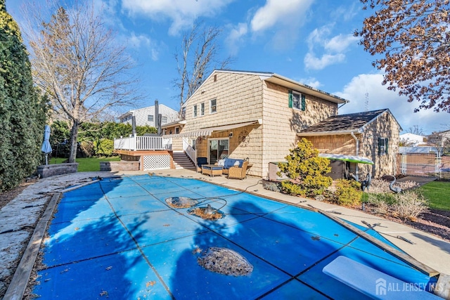 rear view of property featuring a covered pool, a deck, and a patio area