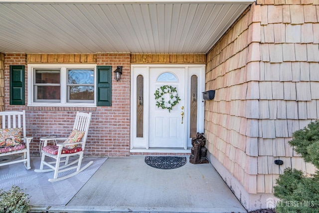 view of exterior entry featuring brick siding and covered porch