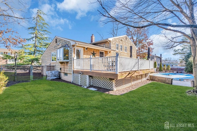 rear view of property with a yard, a deck, a chimney, and a fenced backyard