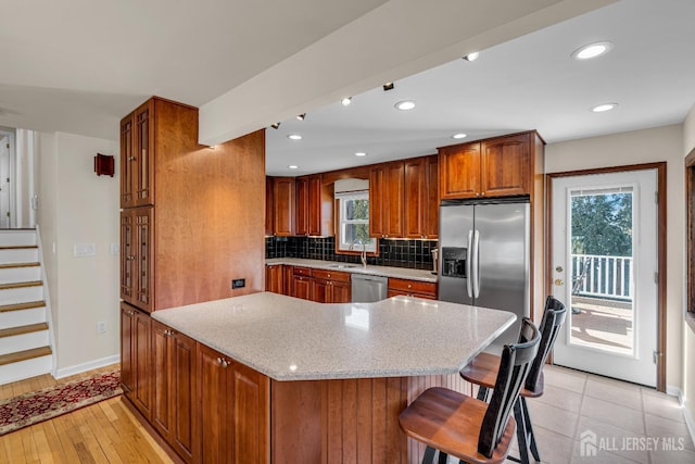 kitchen with light stone countertops, decorative backsplash, brown cabinets, appliances with stainless steel finishes, and a sink