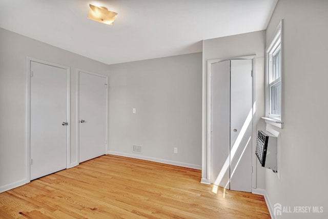 unfurnished bedroom with baseboards, a wall mounted air conditioner, and light wood-style flooring