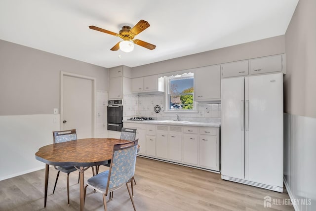 kitchen featuring light wood-style floors, light countertops, black oven, freestanding refrigerator, and a ceiling fan