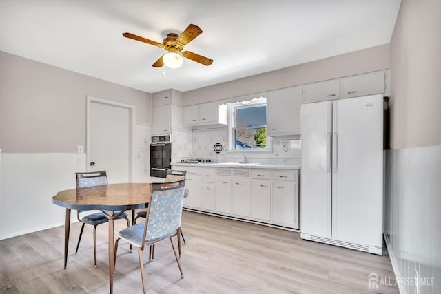 kitchen with freestanding refrigerator, a ceiling fan, oven, light wood-type flooring, and a sink