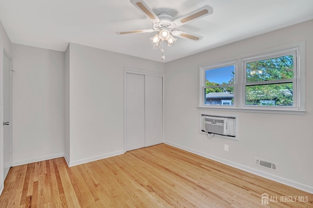 unfurnished bedroom with visible vents, a closet, baseboards, light wood-type flooring, and a wall mounted AC