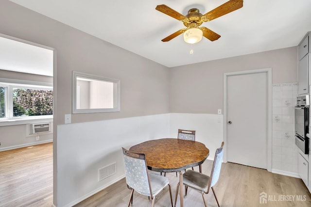 dining space with visible vents, baseboards, ceiling fan, light wood-type flooring, and a wall mounted AC