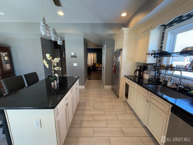 kitchen with sink, appliances with stainless steel finishes, hanging light fixtures, a center island, and cream cabinets