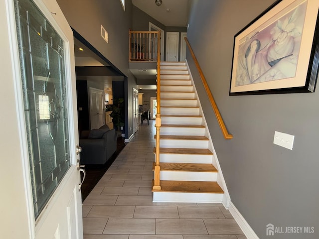 stairway featuring visible vents, baseboards, and a high ceiling