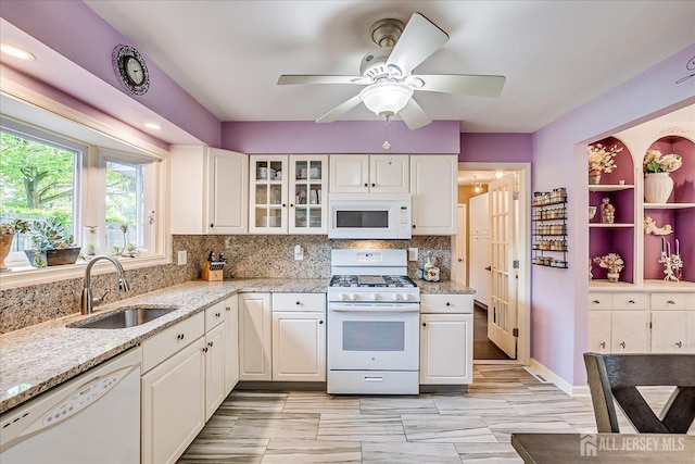 kitchen featuring white appliances, a sink, white cabinets, tasteful backsplash, and light stone countertops