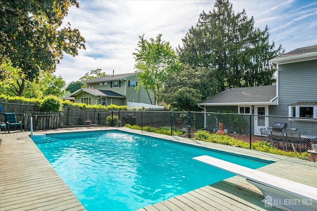 view of pool with fence, a diving board, and a wooden deck