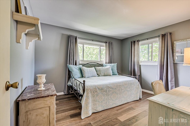 bedroom with multiple windows, wood finished floors, and baseboards