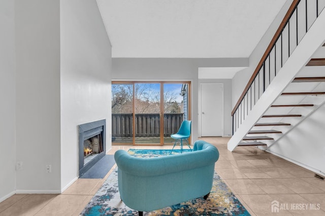 living area featuring a warm lit fireplace, light tile patterned floors, baseboards, and stairs