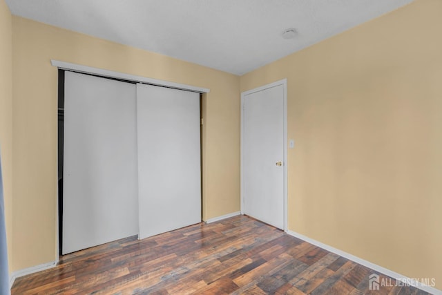 unfurnished bedroom with dark wood-style flooring, a closet, and baseboards