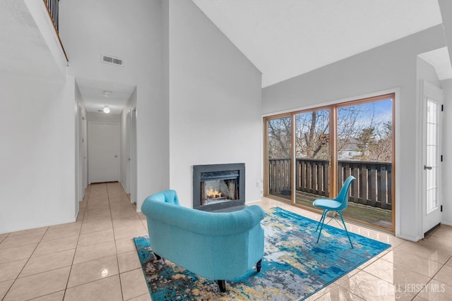 living area featuring high vaulted ceiling, visible vents, a lit fireplace, and baseboards