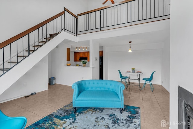 sitting room with a ceiling fan, light tile patterned flooring, a towering ceiling, and stairs