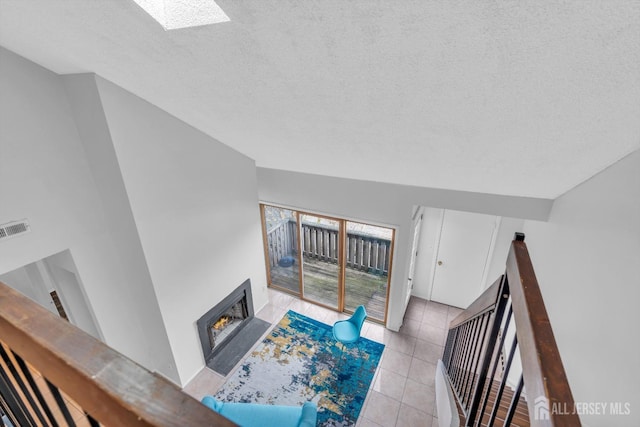 living area with a skylight, light tile patterned floors, visible vents, a textured ceiling, and a lit fireplace