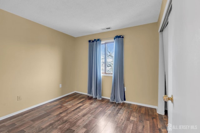 empty room featuring visible vents, dark wood finished floors, a textured ceiling, and baseboards