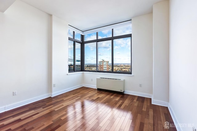 spare room featuring baseboards, wood finished floors, and radiator