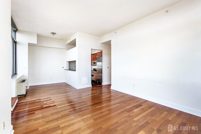 unfurnished living room with radiator, baseboards, and light wood finished floors