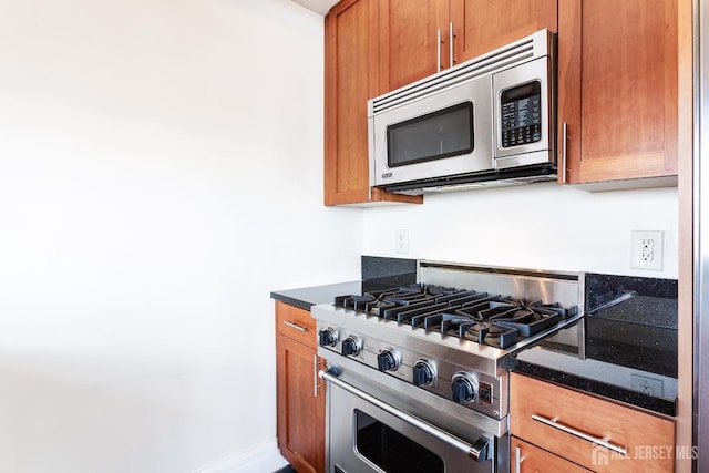 kitchen featuring brown cabinetry, stainless steel appliances, and dark stone countertops