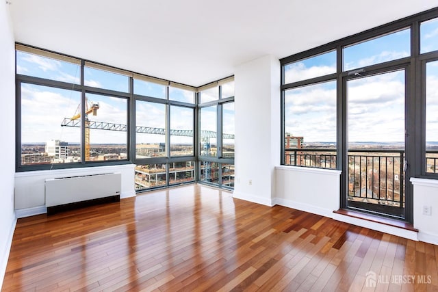 unfurnished room with plenty of natural light, radiator heating unit, baseboards, and hardwood / wood-style floors