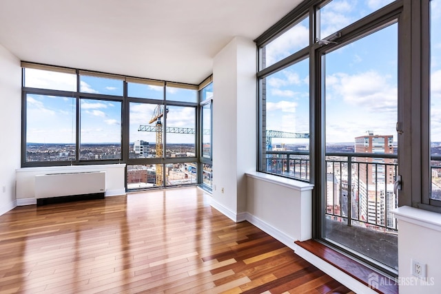 empty room featuring baseboards, radiator heating unit, wood finished floors, and a city view