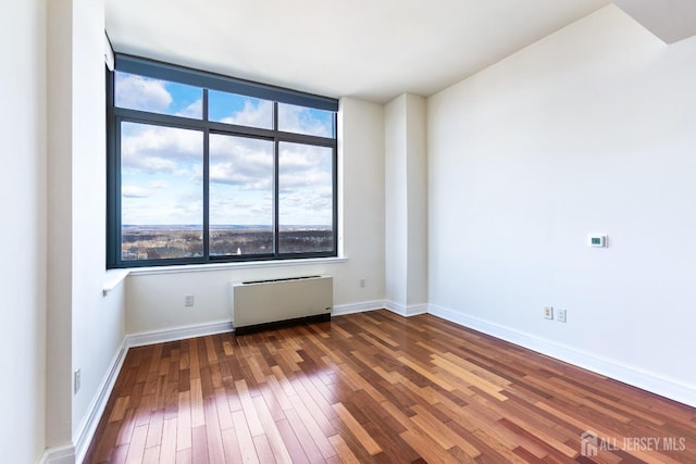 empty room with baseboards, radiator heating unit, and hardwood / wood-style flooring