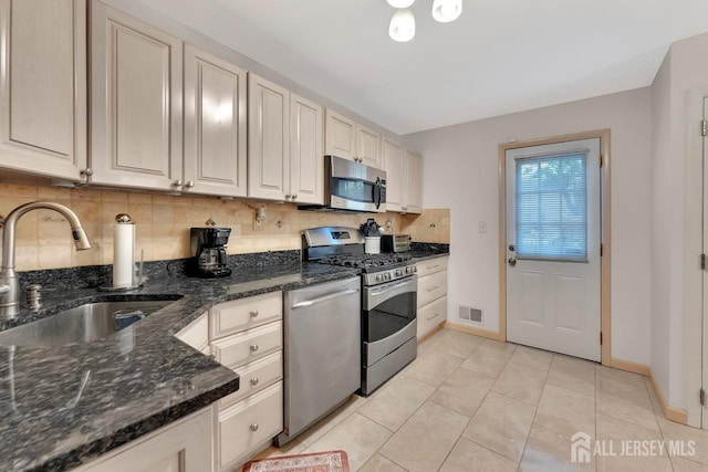kitchen featuring light tile patterned flooring, a sink, stainless steel appliances, backsplash, and visible vents