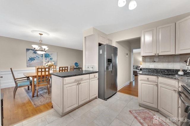 kitchen featuring stainless steel refrigerator with ice dispenser, tasteful backsplash, a sink, a notable chandelier, and decorative light fixtures